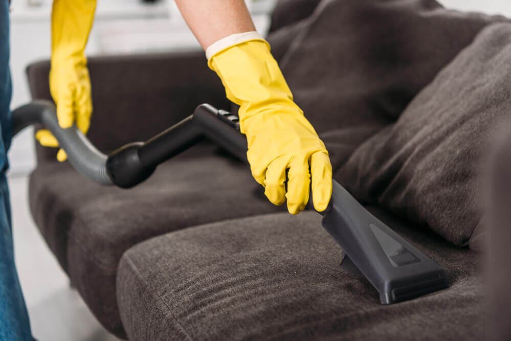 close up of a worker wearing yellow gloves doing some couch cleaning with a wet vacuum