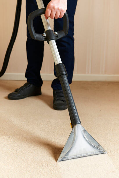 A carpet cleaning Toowoomba worker using a vacuum cleaner to clean some cream carpet