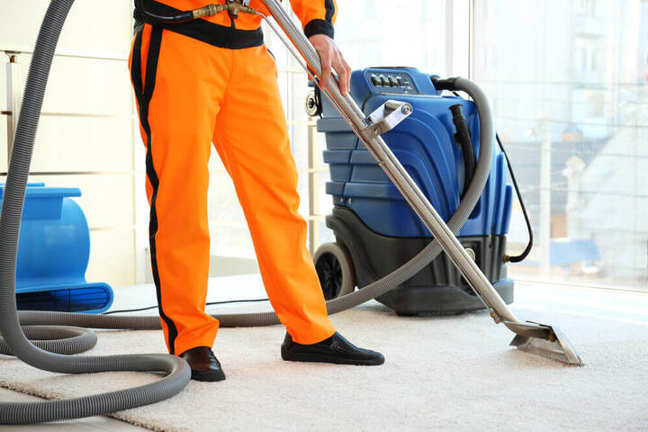 carpet cleaning Toowoomba's worker in orange overalls cleaning a carpet with a wet vacuum cleaner