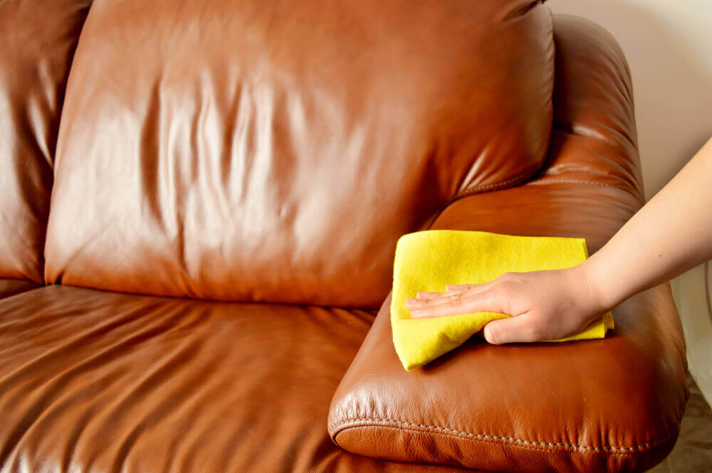 a lounge cleaning worker wiping down a brown leather couch with a yellow cloth