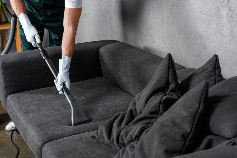 A worker couch cleaning a dark grey couch with gloves on