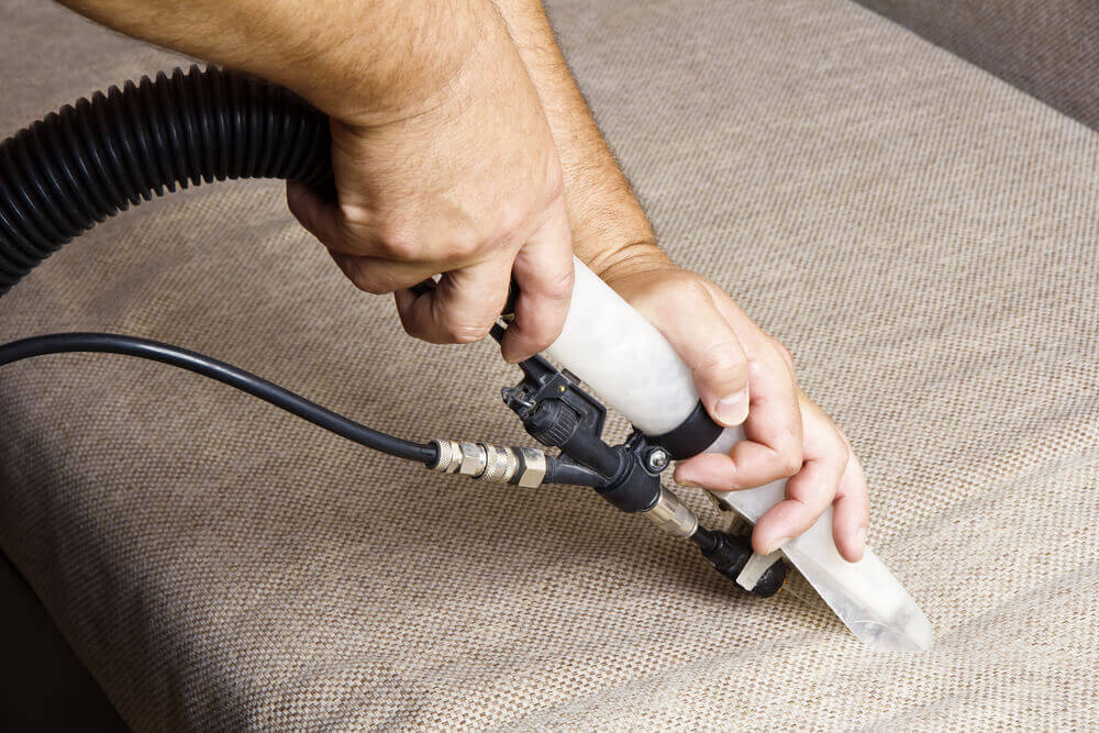 close up of a worker using a wet vacuum upholstery cleaner on a couch and pressing down with two hands